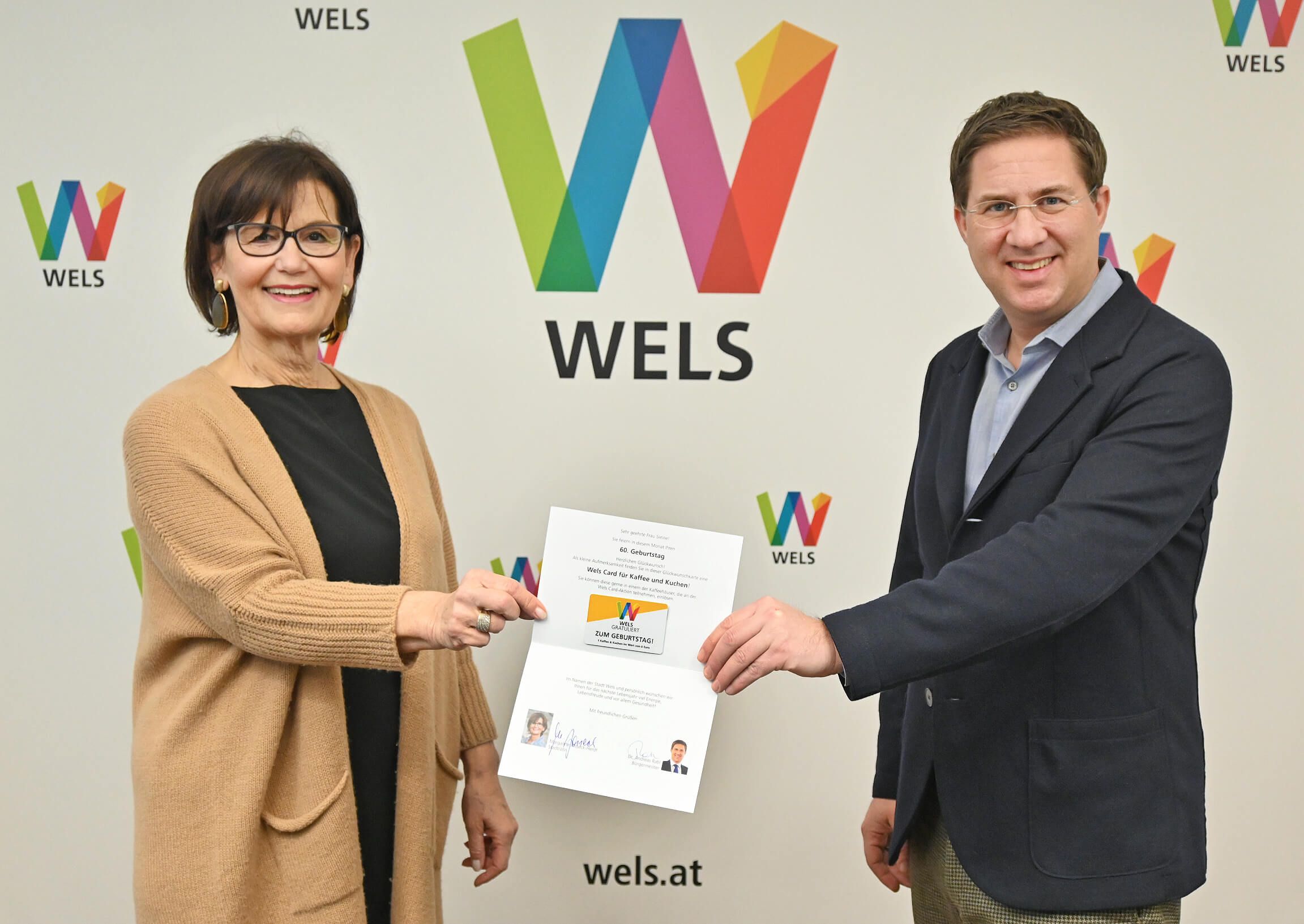 Bürgermeister Dr. Rabl und Stadträtin Josseck-Herdt, Referentin für Generationen, halten gemeinsam mit Abstand eine Geburtstagskarte mit der Wels-Card