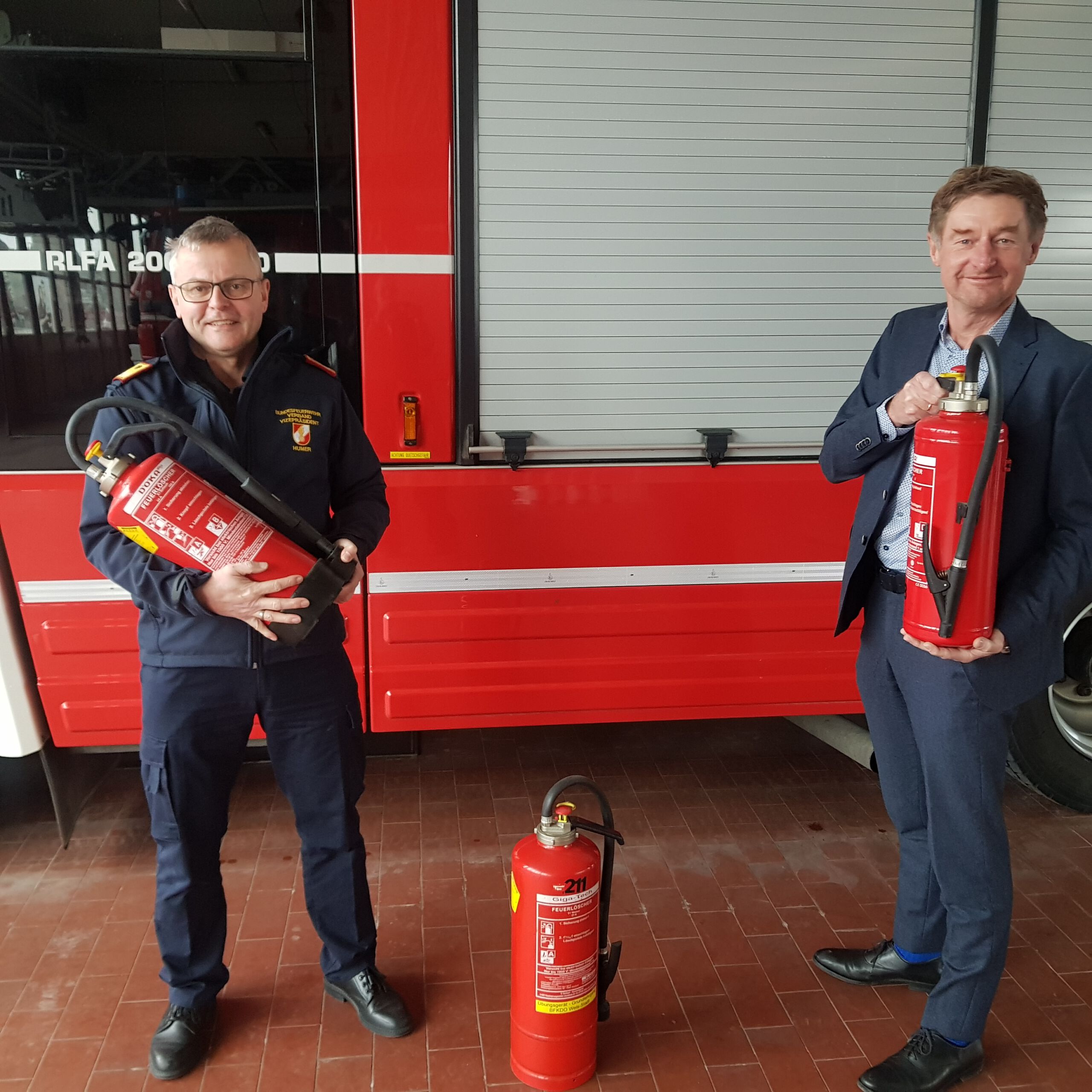 Feuerwehrkommandant Ing. Humer und Vzbgm. Gerhard Kroiß mit Feuerlöschern in der Hand vor einem Feuerwherauto