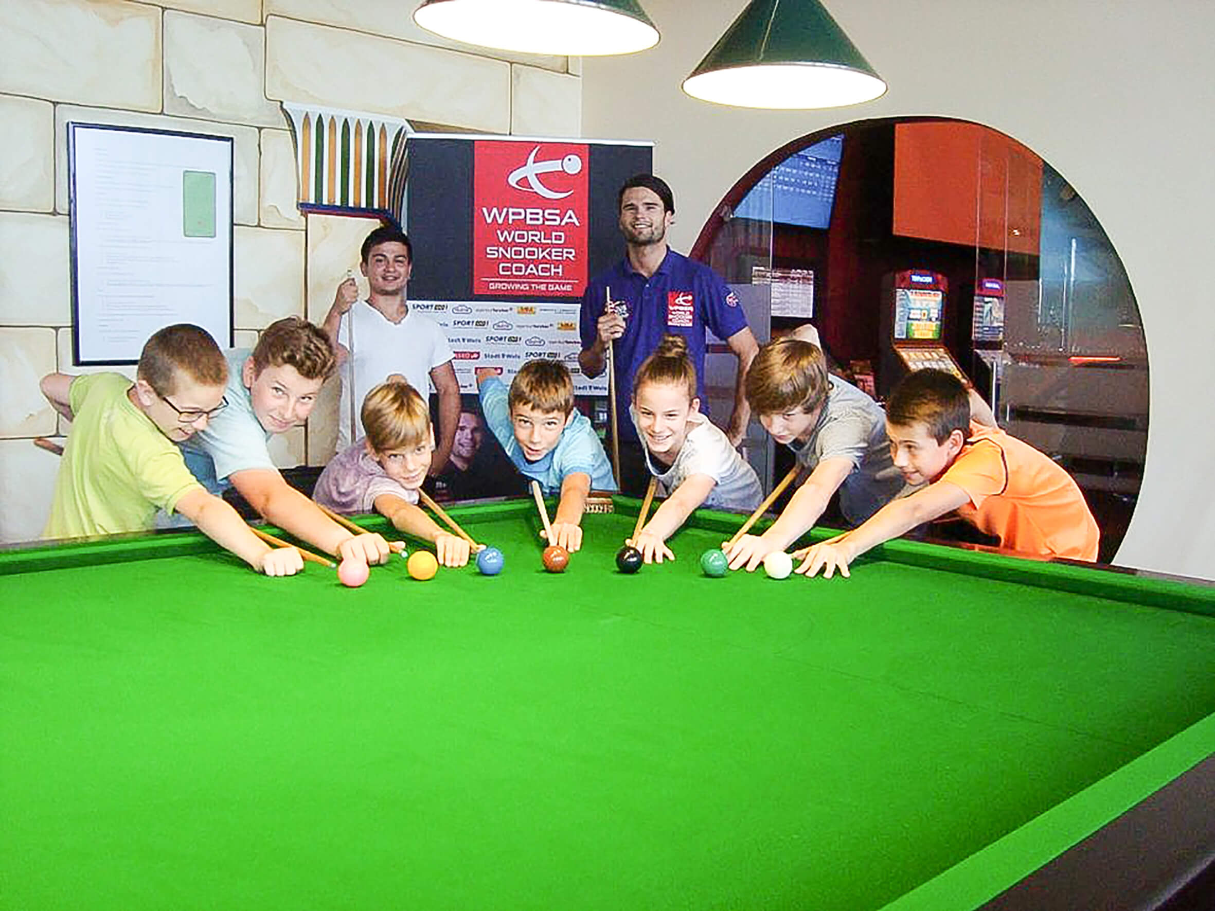 sieben Kinder posieren beim Billiardtisch mit einem Kö und einer Kugel beim Billiardkurs mit den Trainern