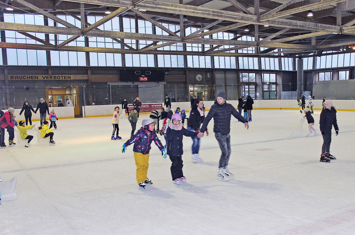 Erwachsene und Kinder die gemeinsam Runden auf dem Eis in der Welser Eishalle ziehen